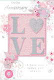 The anniversary card depicted here radiates a gentle, intimate charm, much like a pastel bouquet placed in a bay window of a Crouch End terrace. At its centre, the word LOVE is proudly displayed in embossed capital letters, each one covered with a fine layer of sparkling, frosted glitter. This glitter gives the lettering a slightly raised, grainy texture and a delicate, pearly shine, as if dusted with morning light over Alexandra Palace in the distance. The glittered word rests on a central rectangle of blush pink, a tone richer than the surrounding background, drawing the eye immediately. Beyond this focal block, the background colour softens into pale pink and almost white, creating a soft, luminous field. From the corners and outer edges, stylised floral motifs curl inward. These flowers and leaves are rendered in slender, flowing lines of soft grey and white, with tiny silver highlights that glint like delicate jewellery. The blossoms are small and graceful, undefined enough to feel like imagined flowers yet clear in their petal and leaf shapes, drifting in loose, swirling patterns that echo the natural movement of stems arranged by hand in a Crouch End flower shop. Curving tendrils, dotted clusters, and fine loops add rhythm and motion around the central word without overwhelming it. Above and below the floral sweep, an elegant script in muted grey carries the anniversary message in a light, flowing style that complements the curves of the illustration. Altogether, the card conveys a sense of tenderness, serenity, and quiet joy, as if it has been created to partner perfectly with a soft-toned anniversary bouquet delivered to a doorstep near Crouch Hill or Weston Park.